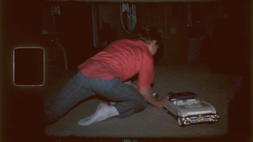An adult playing with a ball and baby near a toy car on the living room floor