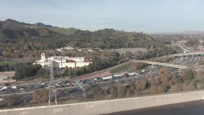 A congested freeway bordered by a large building with a prominent clock tower surrounded by hills and vegetation