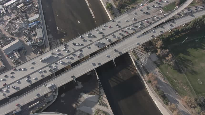 A busy highway interchange with cars flowing across bridges over a river set against a backdrop of industrial and urban development