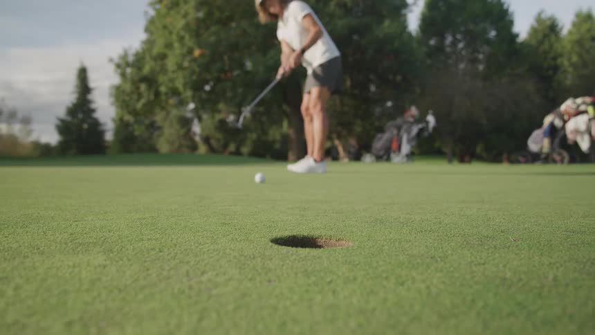 Woman hits the golf ball into the hole on the putting green