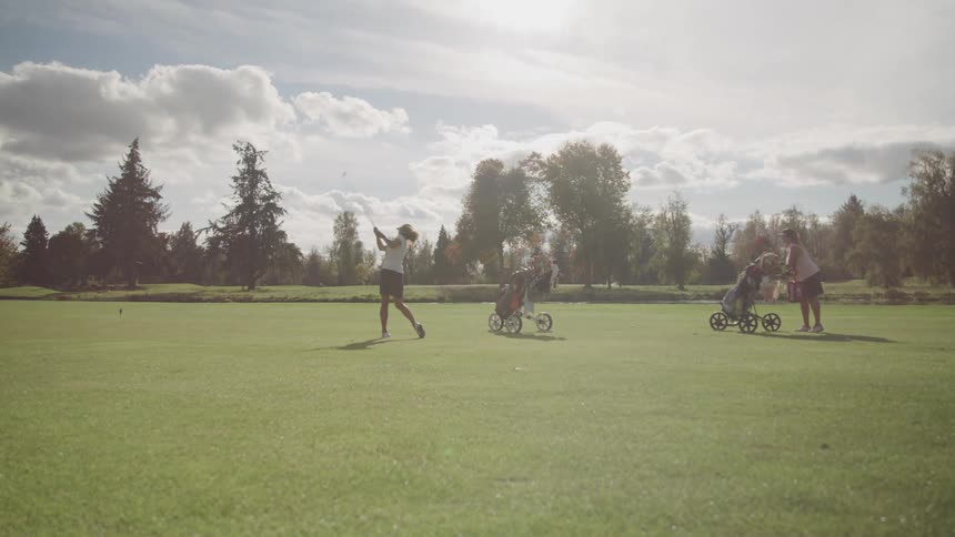 Woman swings her golf club while another waits for her turn on the golf course