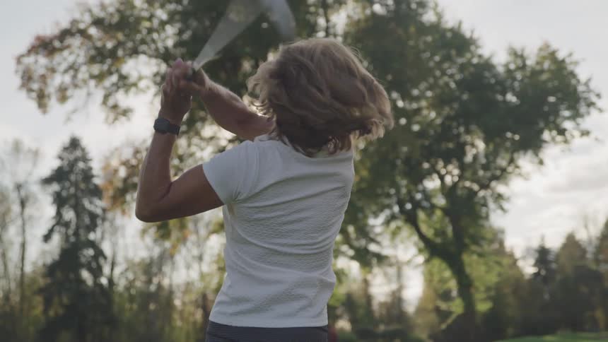 A woman wearing a visor swings a golf club