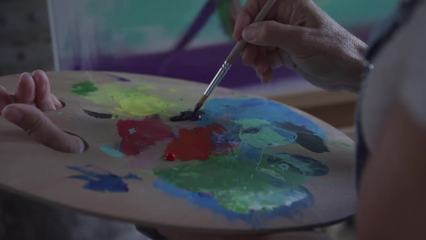 Hand with a brush taking colors from a palette
