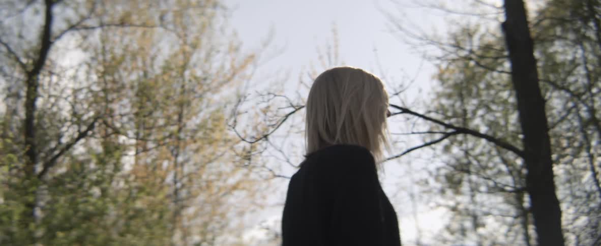 Blond woman walks through trees as the sun shines