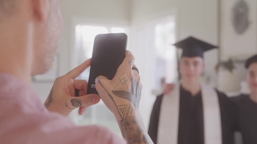 A father takes a photo of his son who is graduating