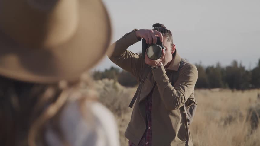 Photographer standing in a field takes a picture of a woman on an autumn day