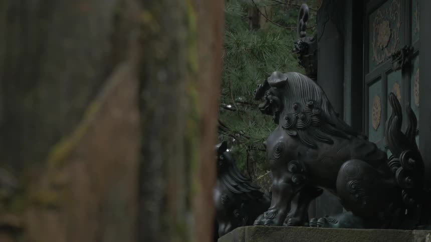 Two statues guard a structure surrounded by trees