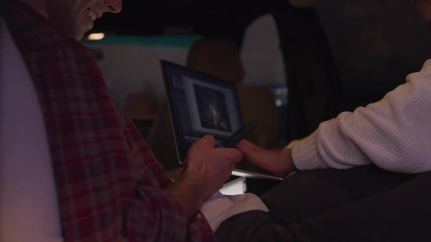 Man scrolls on his smartphone while his travel mate works on a laptop