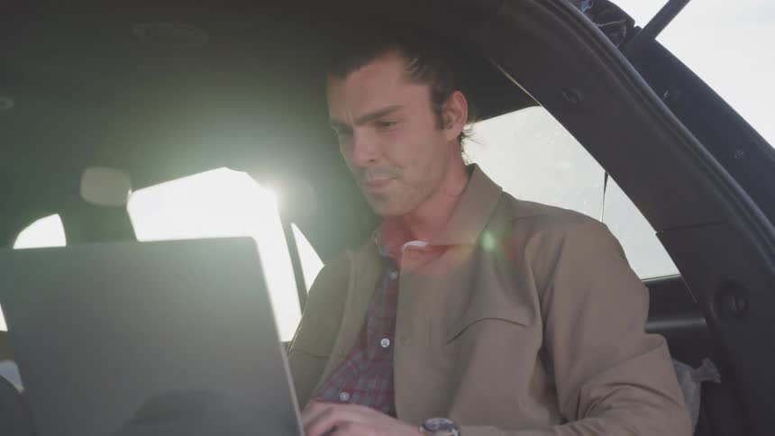 Boy sitting in car typing on computer and happy