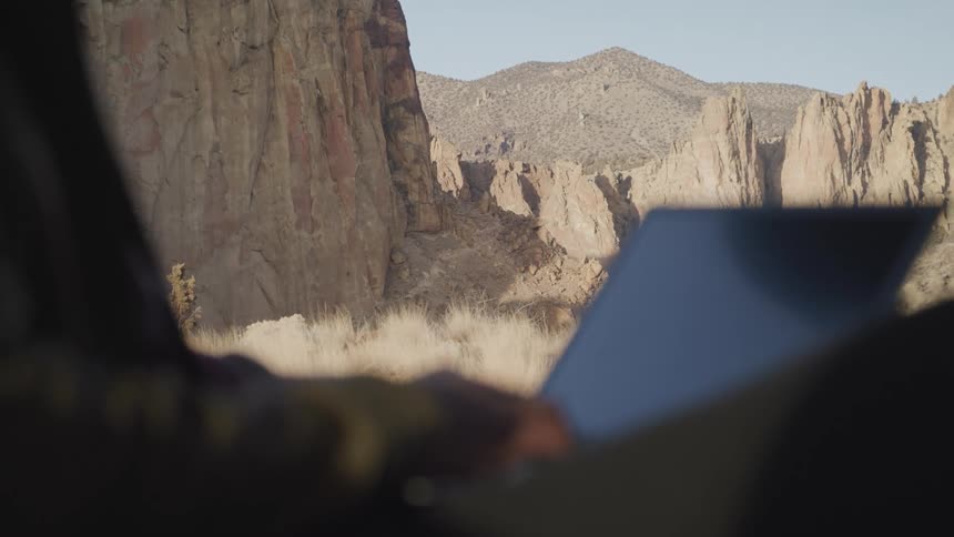 Boy typing on computer on a mountain landscape