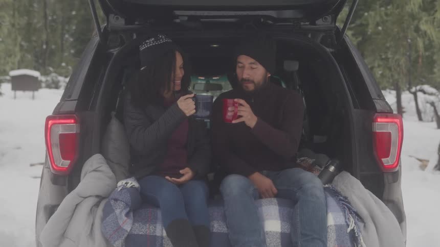 Couple tailgating in snow covered wilderness toasting with a cup of coffee