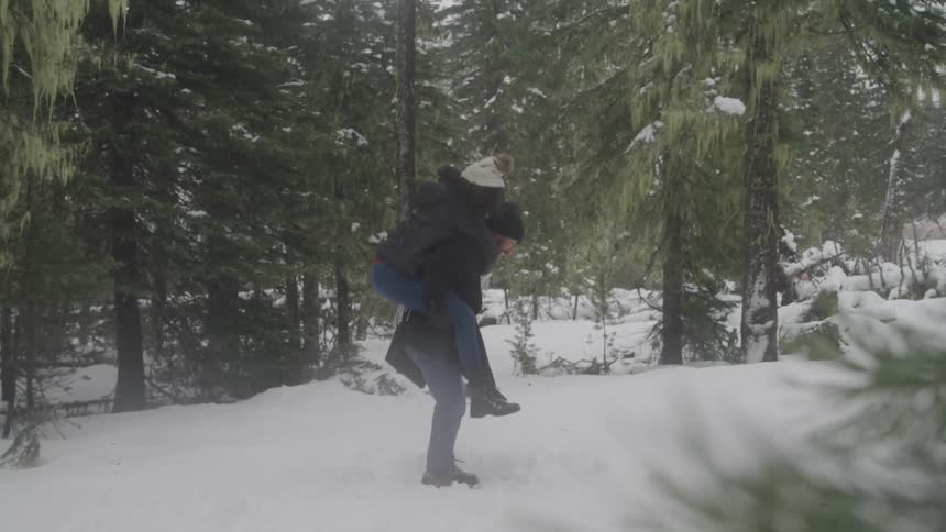A man carries a woman on his back in the snow as they laugh