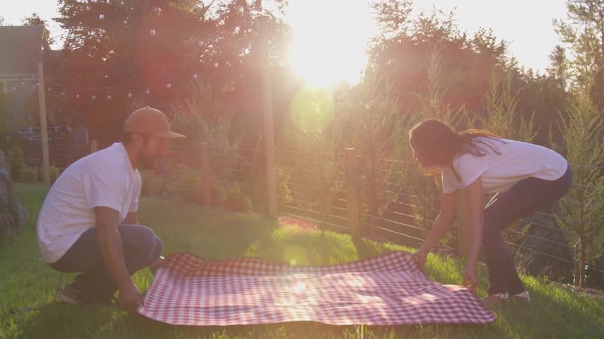 A man and woman set a picnic blanket in the park