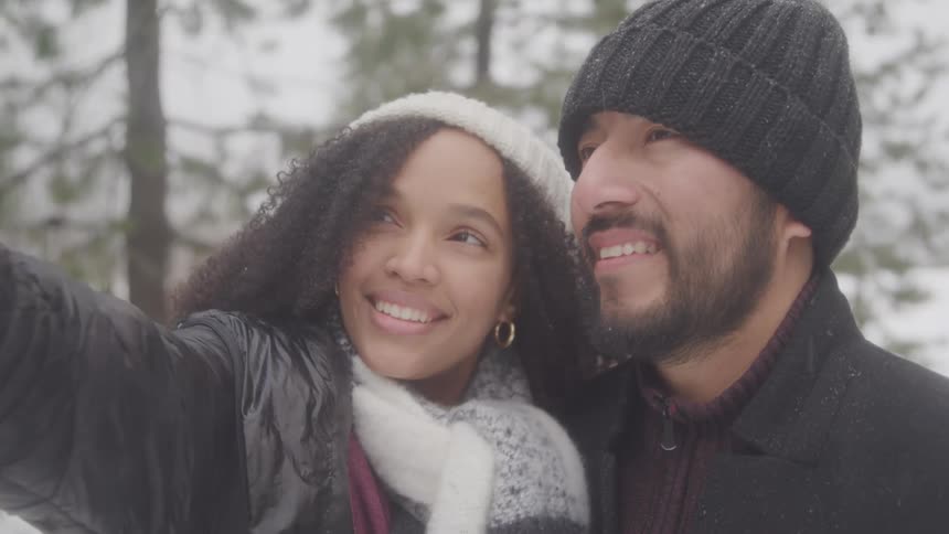 Couple take a selfie together near trees on a snowy winter day