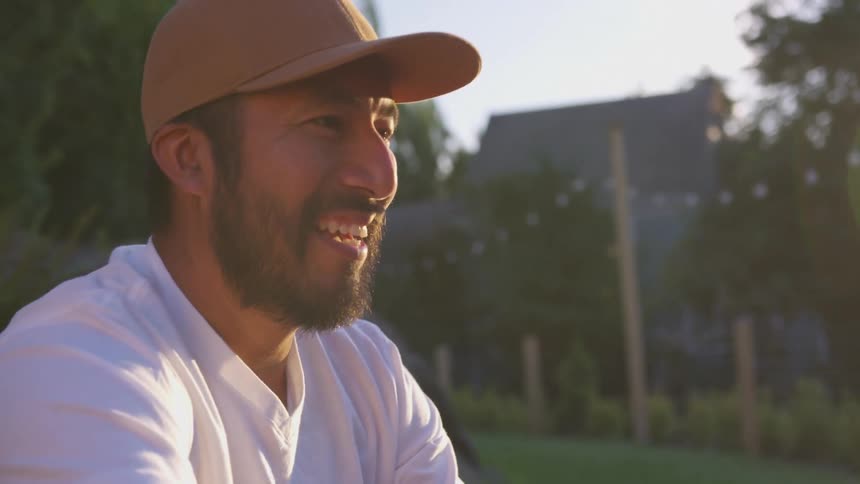 Man in a hat smiling with a neighborhood in the distance