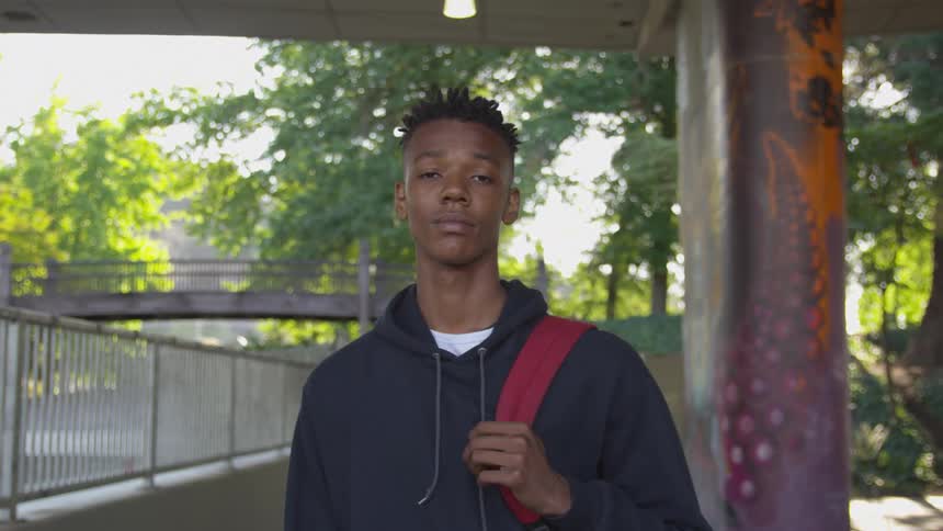 A teenager is holding a backpack strap outside