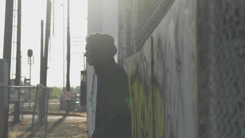 Boy in a sweatshirt leaning against a wall looking up