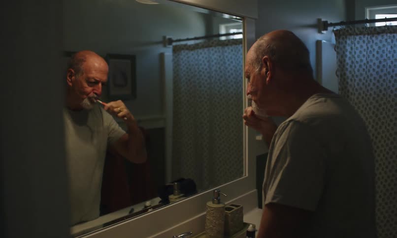 Man brushing his teeth in the bathroom mirroring himself