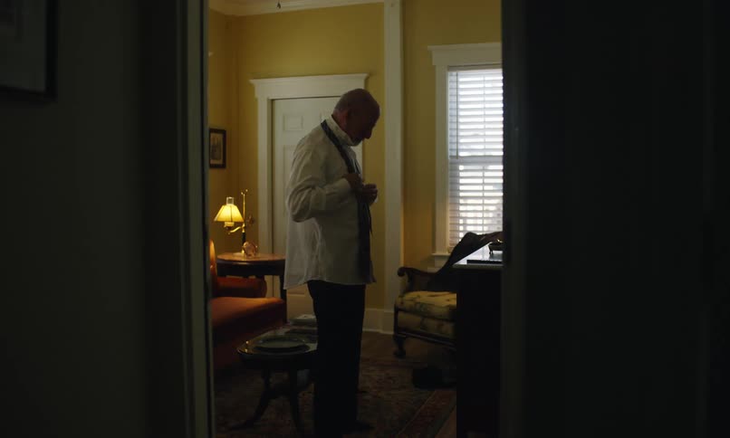 Elderly man inside a room dressing up by putting on a tie