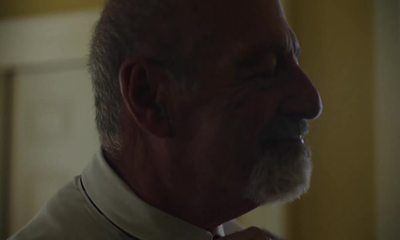 Man adjusts his tie and his shirt collar in a dark room