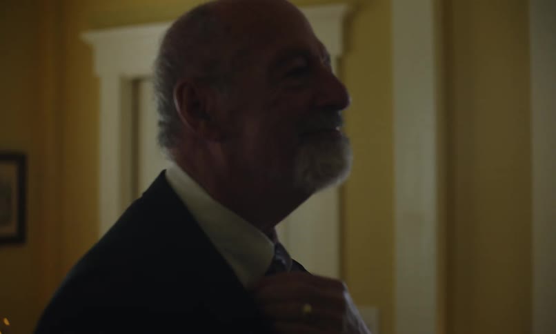 Man smiles as he puts on a suit jacket and adjusts his tie