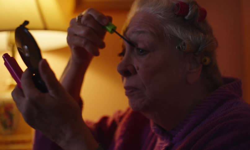 An elderly woman is applying makeup on her face