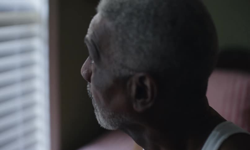 An older man is sitting and looking out a window