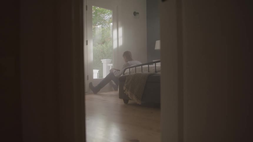 A man is sitting on the floor by his bed