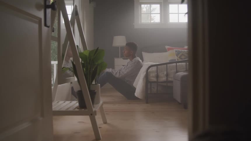 Sad man sits on the floor leaning against the side of the bed