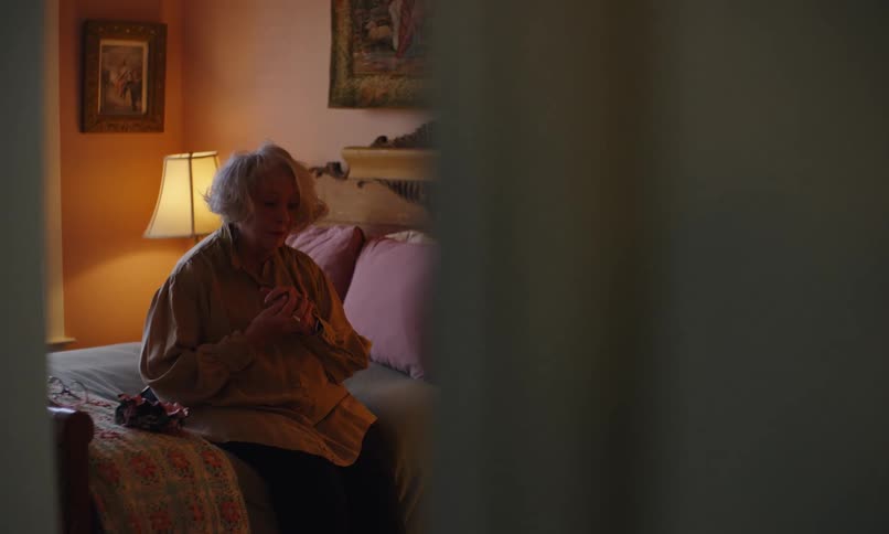 A woman clasps her hands while sitting on her bed