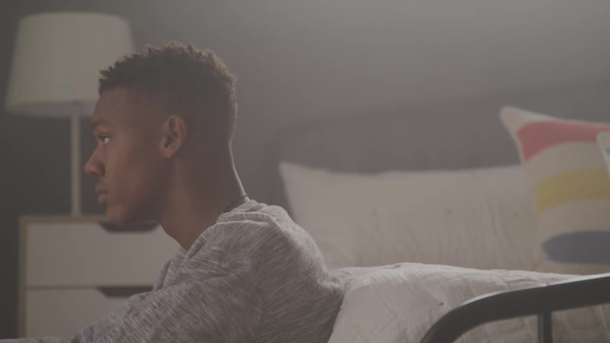 Boy leaning against the bed looking up