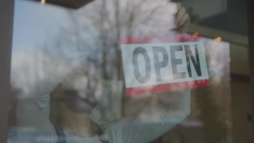 A masked employee turns the closed sign over to show an open sign