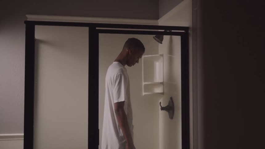 A teenager is standing in the shower with his shirt on