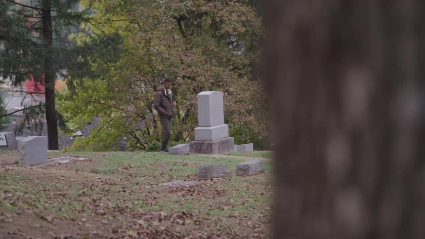 A teenager is standing in front of the tombstone at the graveyard