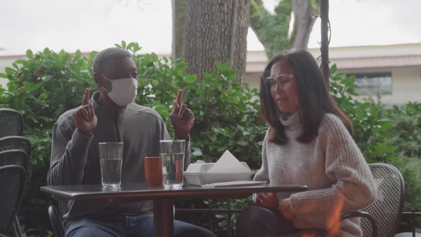 The man and woman are sitting at the table with glasses in front of them and they are talking