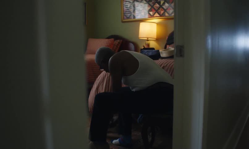 An elderly man is sitting on a chair in his bedroom putting on shoes