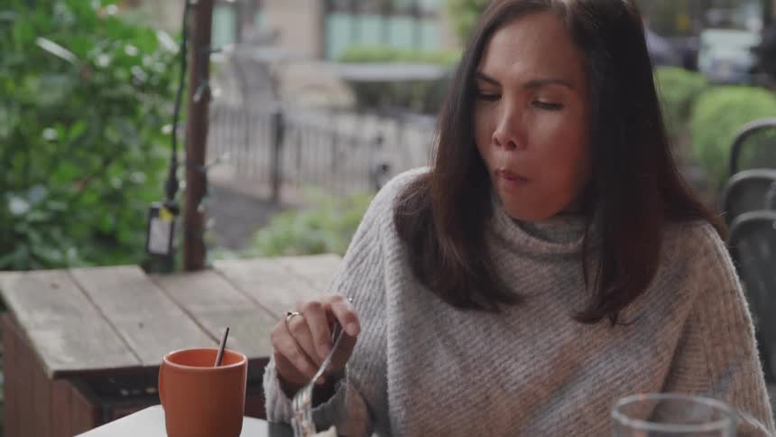 Woman sitting at an outdoor restaurant patio eating a slice of cake