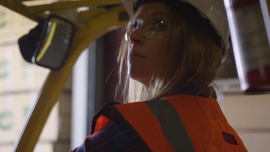 Woman in a hardhat sits in a forklift and looks over her shoulder