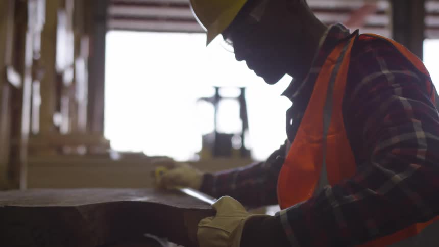 Man uses a measuring tape on lumber in an open warehouse