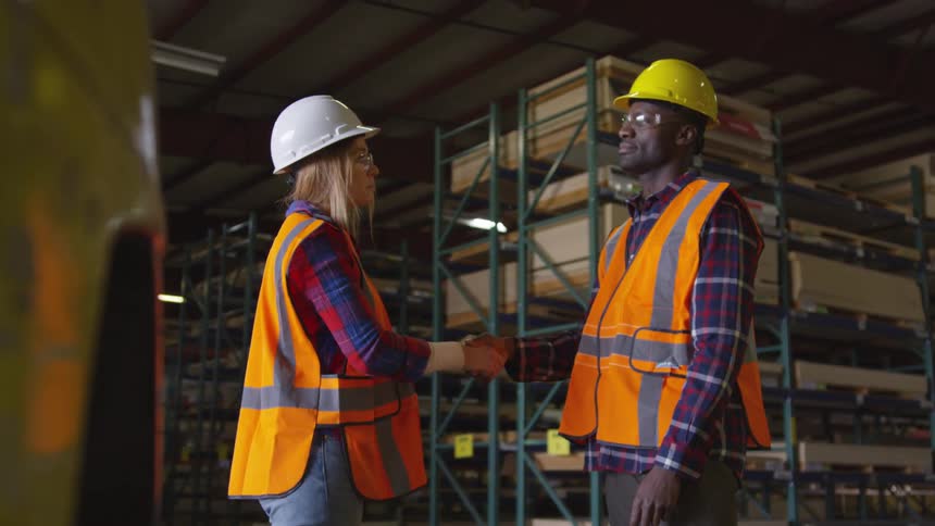 Two workers shake hands by the lumber storage