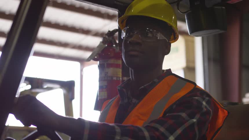 The black man is driving the equipment inside a warehouse