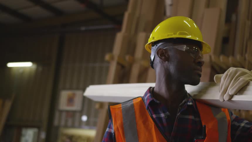 Man in a warehouse carrying lumber on his shoulder