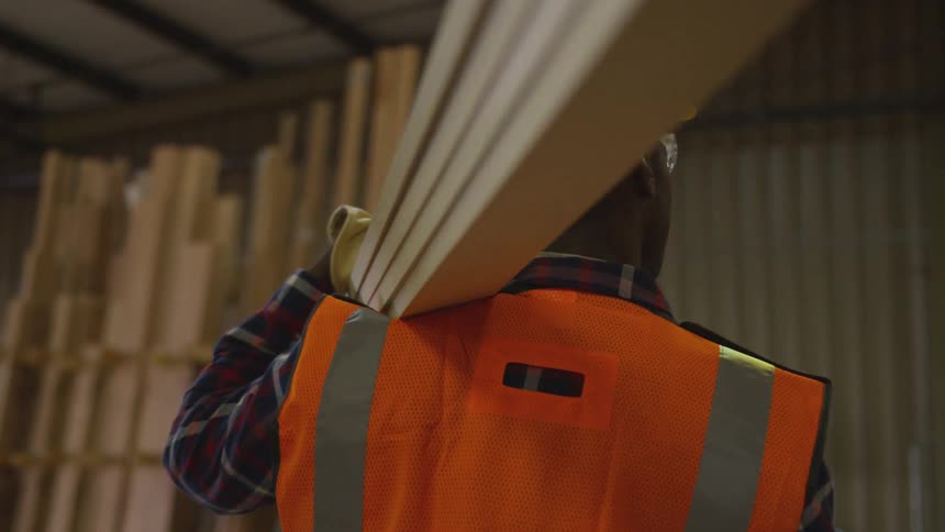 A worker is carrying a stack of wooden planks