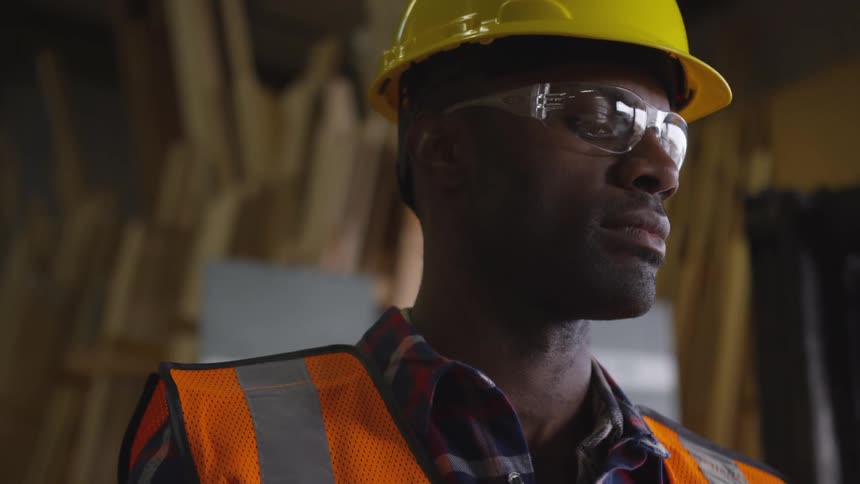 Man in a hardhat and safety gear looking down slightly in a warehouse