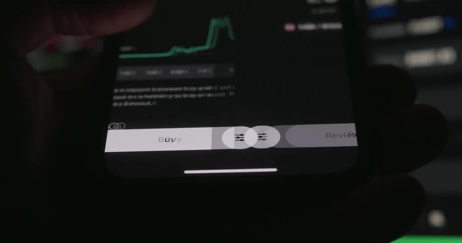 A person presses the buy button on a mobile trading app triggering a transition to the order review screen beneath a rising financial chart