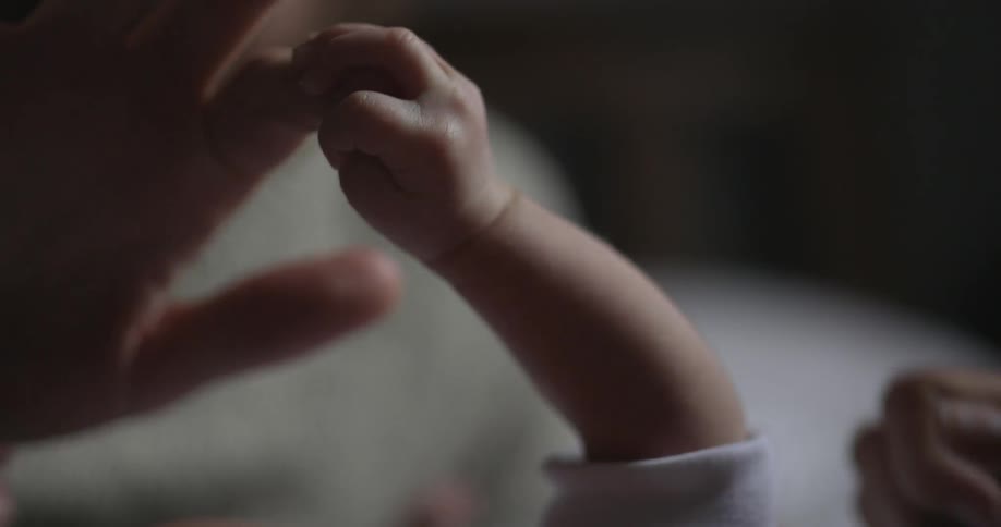 A baby holding on to adult's fingers