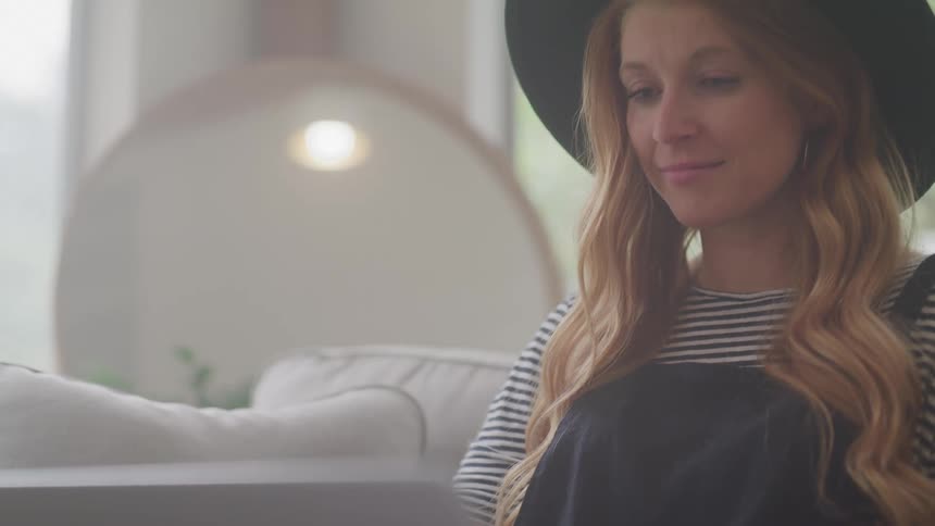 Woman sitting on a couch with a laptop smiles as she types