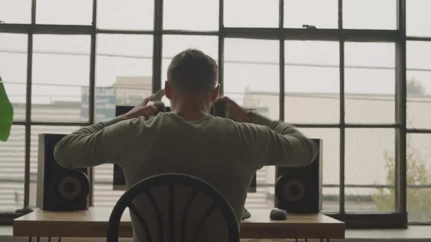 Man walks to his desk and puts on headphones before sitting down in front of his computer
