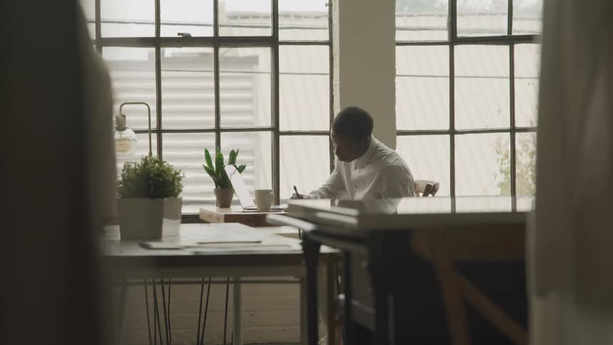 Woman walks through the office while a male coworker writes at a table