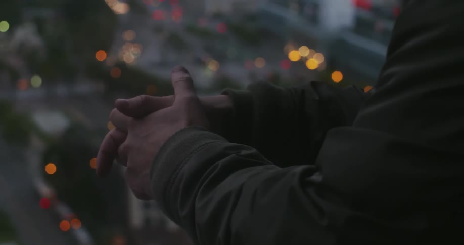A man stands overlooking a city with his hands clasped